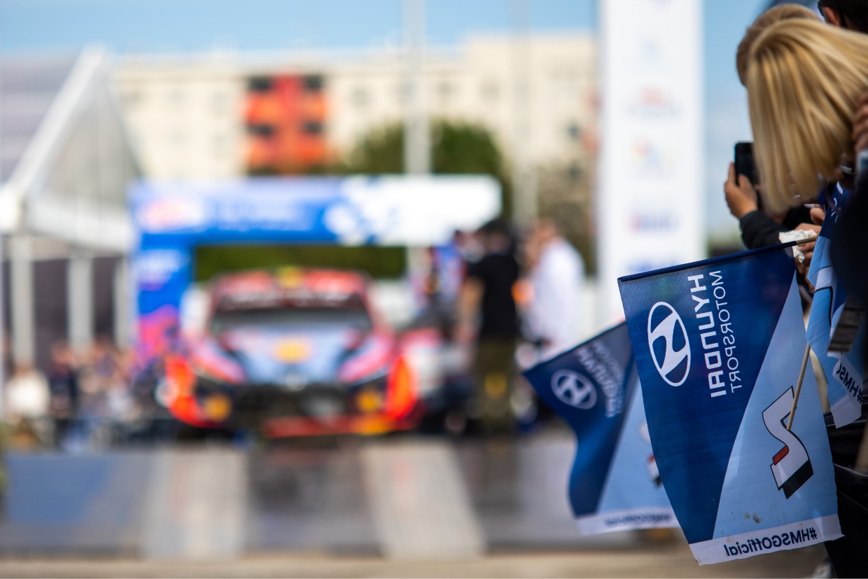 A rally fan cheering for the Hyundai World Rally team takes a picture of a racing car