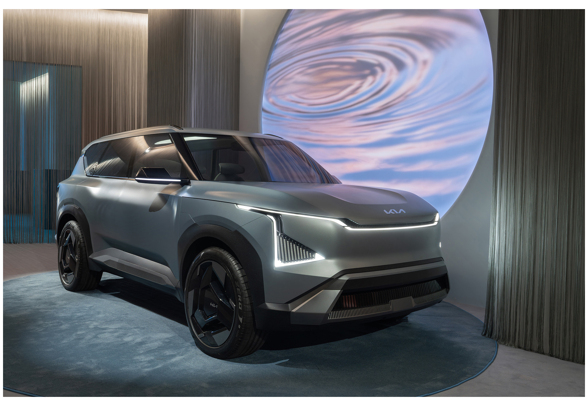 An SUV on display inside an exhibition hall with a circular graphic projected on the wall behind it (EV5)