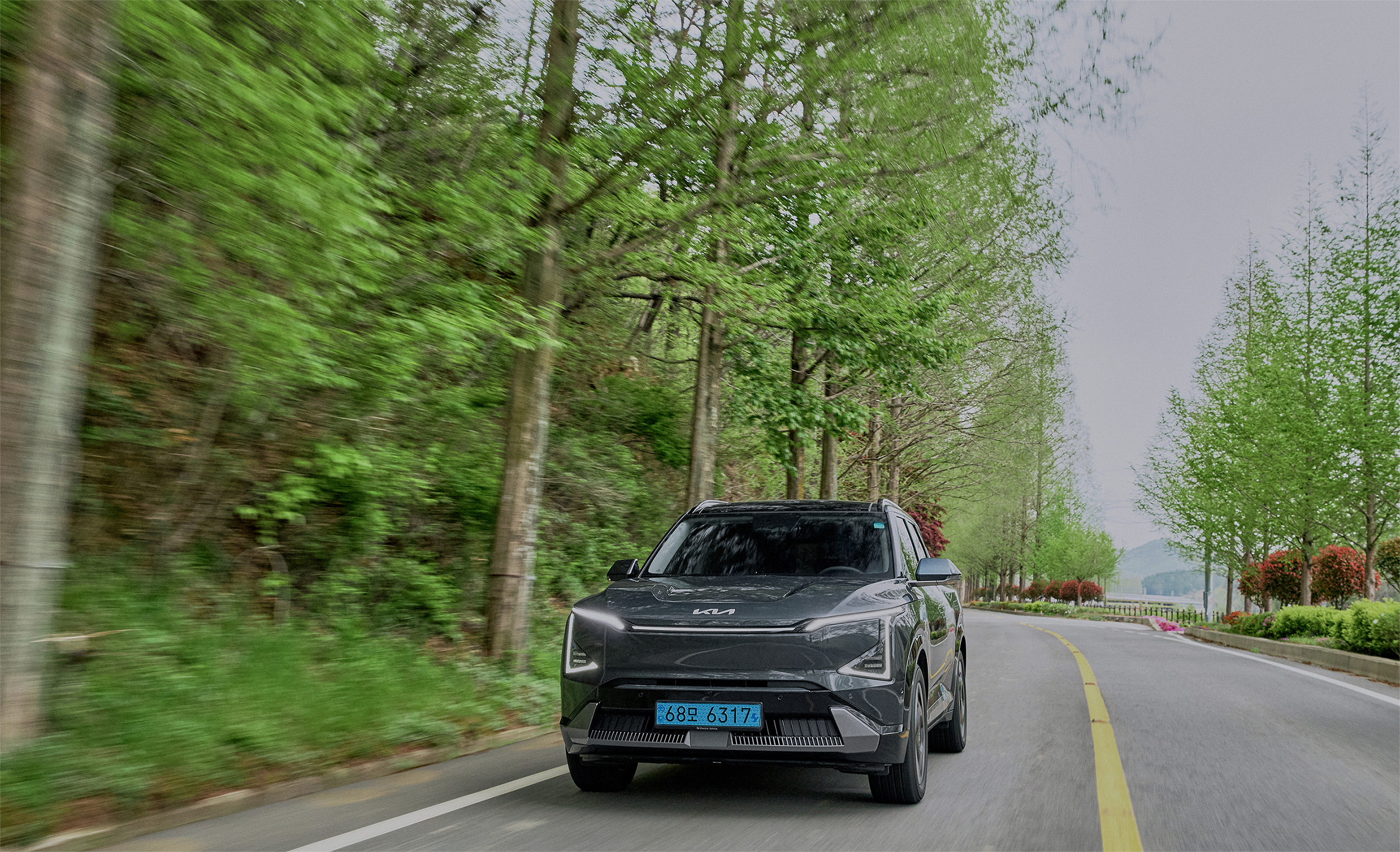 Kia EV5 driving along a forest-lined road