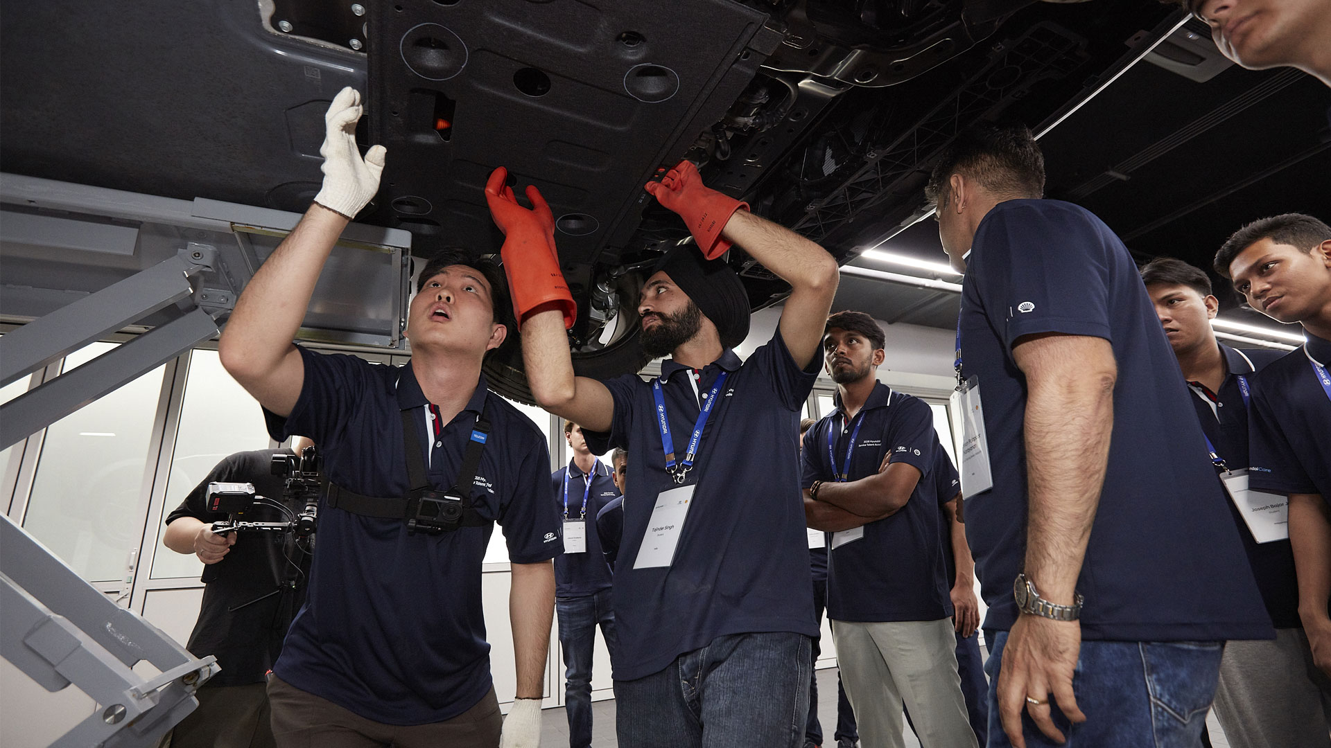 Participants inspect the underside of a vehicle raised on a lift