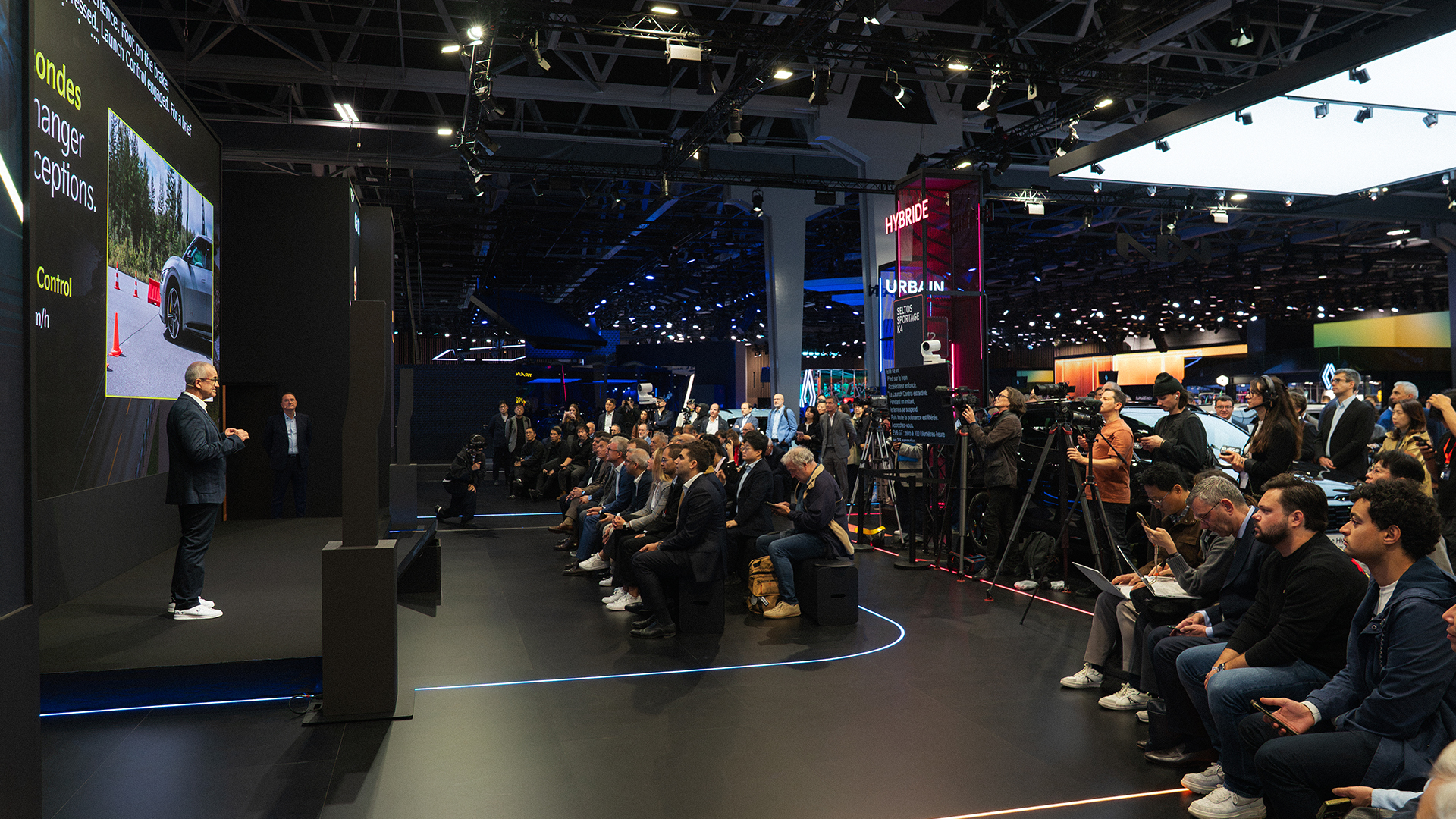 Kia presenter, media crew and audience beside driving footage screen